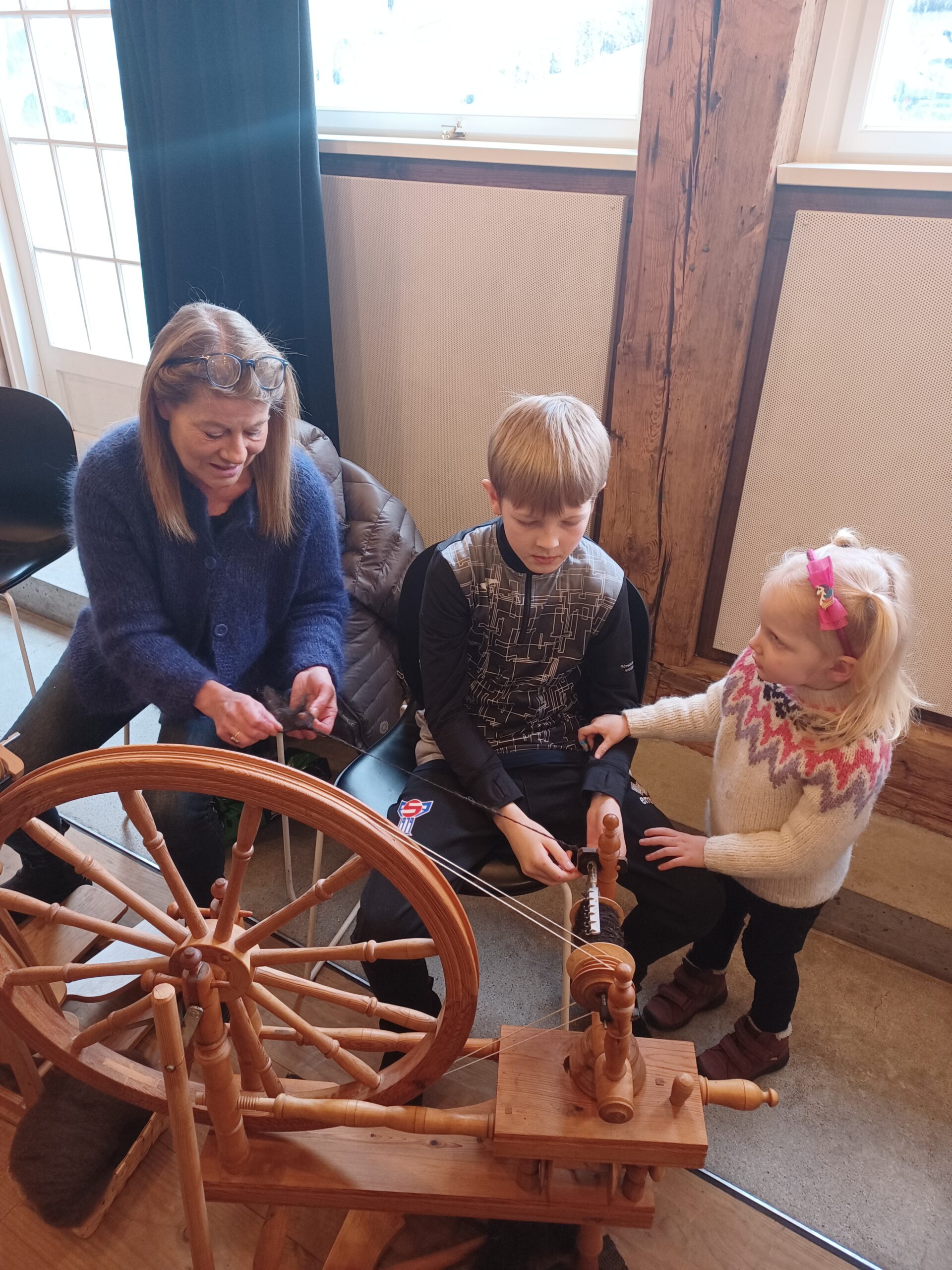 Two children spinning wool with the help of a woman.