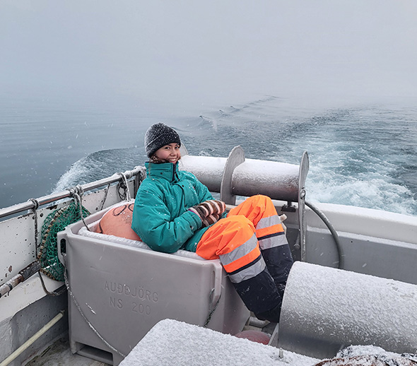 A young woman smiles to the camera sitting half-sunk into the ice box on a fishing boat.